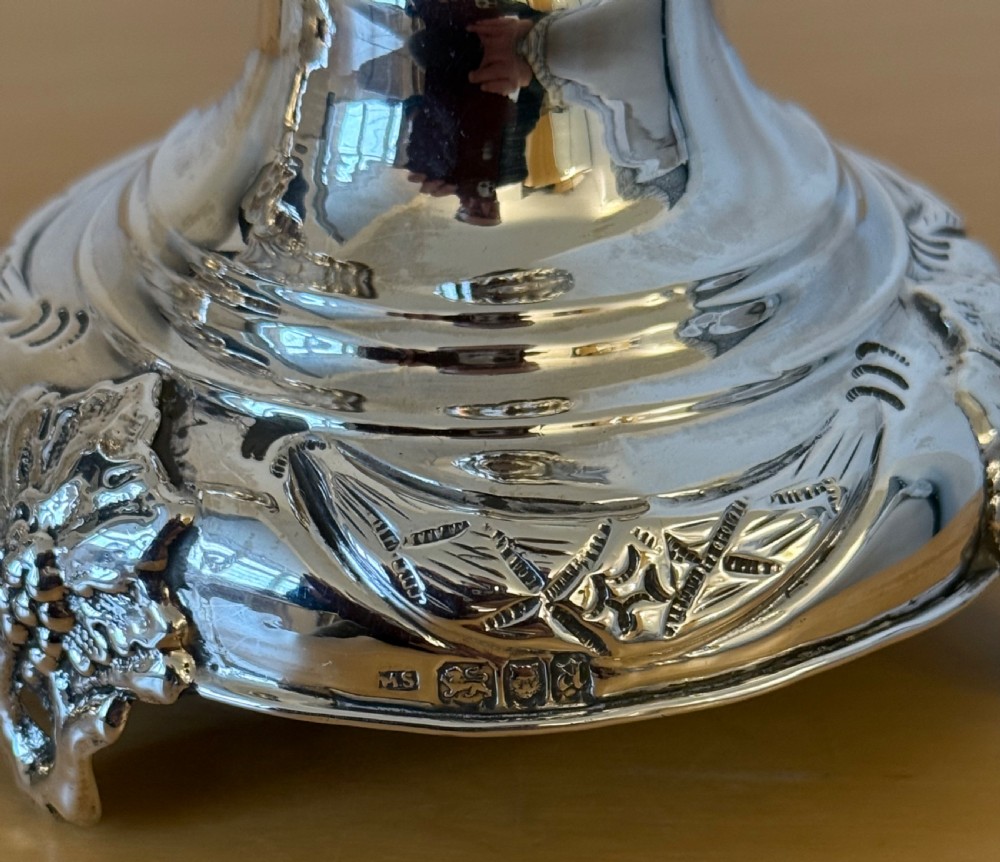 A pair of tall, polished sterling silver Shabbat candlesticks featuring ornate knopped stems and repousse foliate bases. View IX