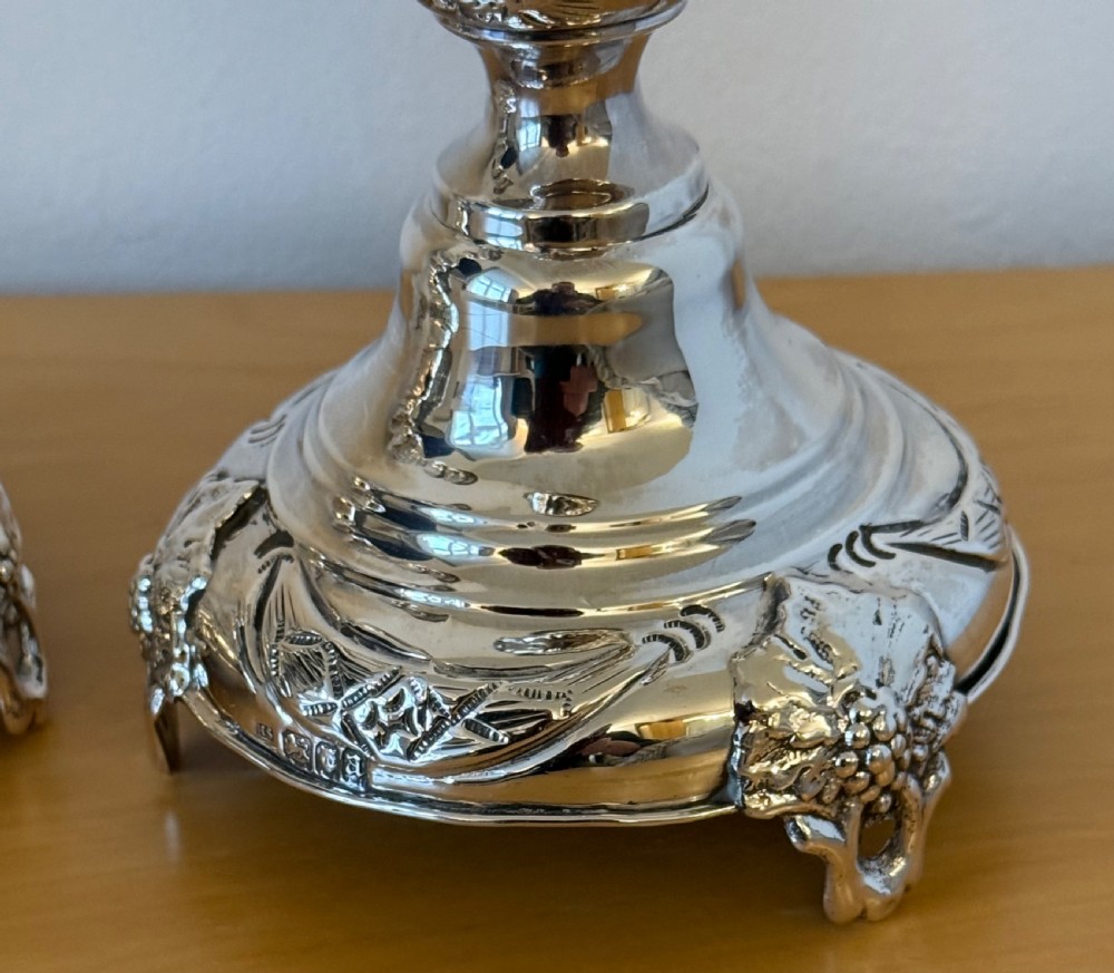 A pair of tall, polished sterling silver Shabbat candlesticks featuring ornate knopped stems and repousse foliate bases. View X