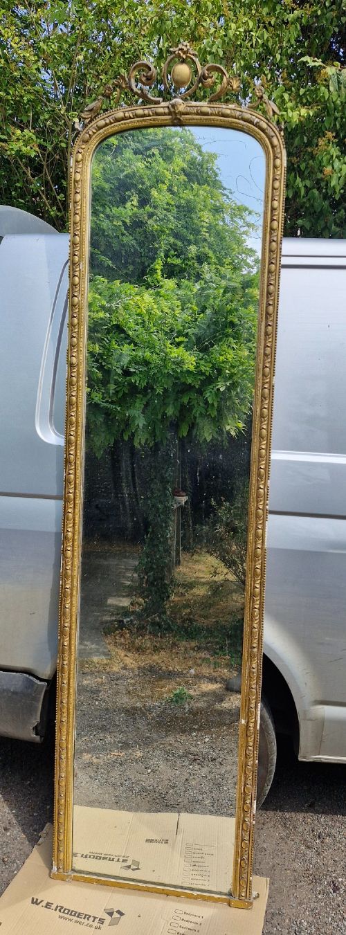 A tall Victorian mirror featuring an arched giltwood frame decorated with bead moulding and an ornate cresting motif at the top. View VII