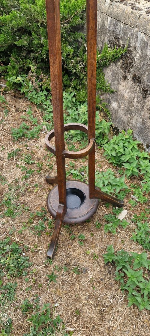 A tall Edwardian dark oak coat stand featuring brass hooks, a turned wooden central column, a lower umbrella retaining ring, and a circular drip tray base. View V
