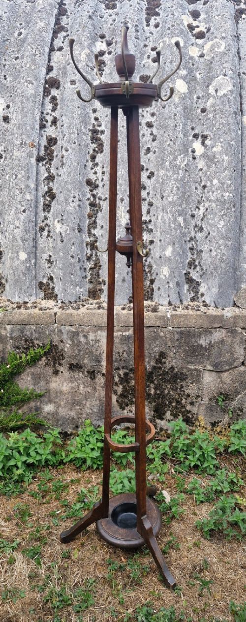 A tall Edwardian dark oak coat stand featuring brass hooks, a turned wooden central column, a lower umbrella retaining ring, and a circular drip tray base. View II