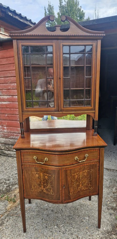 An Edwardian inlaid mahogany two-part display cabinet featuring a swan-neck pediment, glazed upper doors, a mirrored splashback, and lower cupboard doors with floral marquetry. View XV