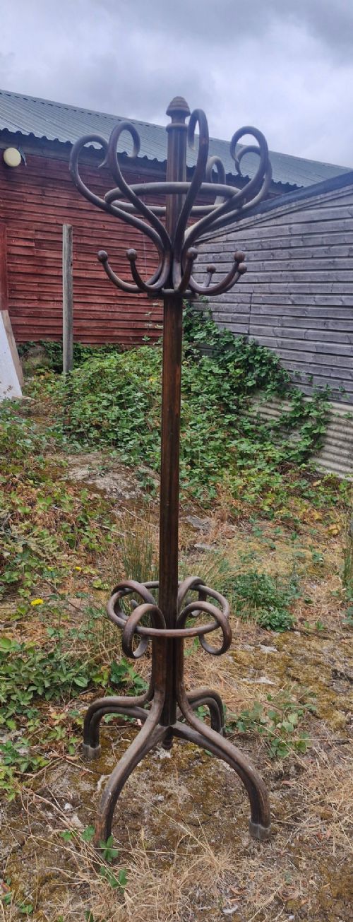An early twentieth-century dark brown bentwood freestanding hat and coat stand featuring scrolled upper hooks, a mid-height umbrella ring, and splayed legs.