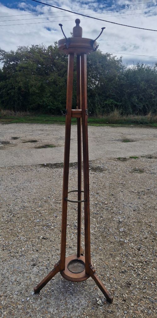 An Edwardian freestanding oak hat and coat stand featuring a revolving circular top with metal hooks, tapered tripod legs, and a bottom umbrella drip tray. View III