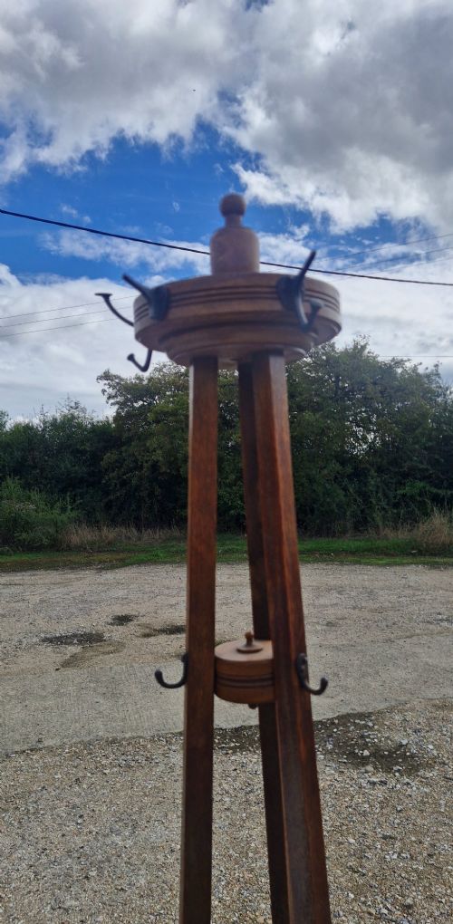 An Edwardian freestanding oak hat and coat stand featuring a revolving circular top with metal hooks, tapered tripod legs, and a bottom umbrella drip tray. View VI