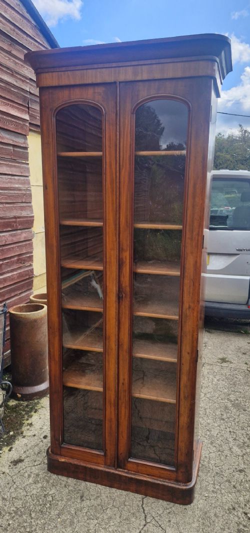 A tall Victorian mahogany bookcase cabinet featuring two arched glazed doors revealing adjustable interior shelving atop a solid plinth base. View VI