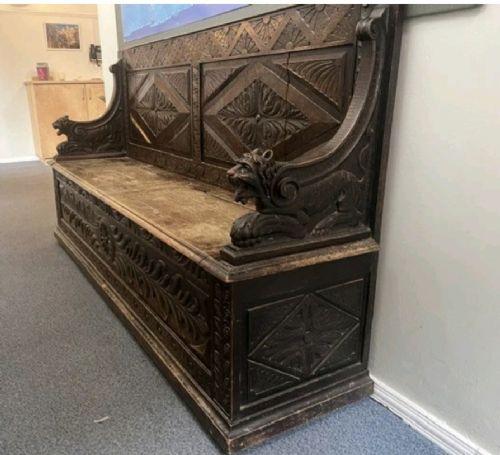 A large Victorian carved dark oak hall bench featuring a high panelled backrest with relief carving and carved lion mask armrests. View IX