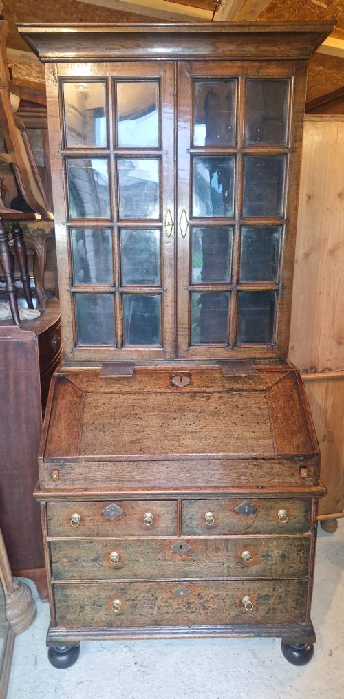 An antique oak bureau bookcase featuring a two-door glazed upper section, a slant-front writing desk, candle slides, and lower drawers raised on bun feet. View VIII