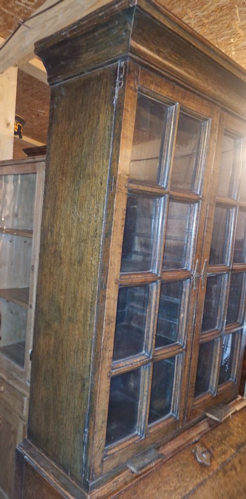 An antique oak bureau bookcase featuring a two-door glazed upper section, a slant-front writing desk, candle slides, and lower drawers raised on bun feet. View IX