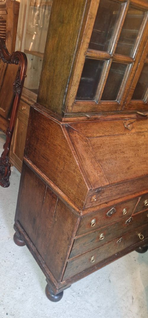 An antique oak bureau bookcase featuring a two-door glazed upper section, a slant-front writing desk, candle slides, and lower drawers raised on bun feet. View X