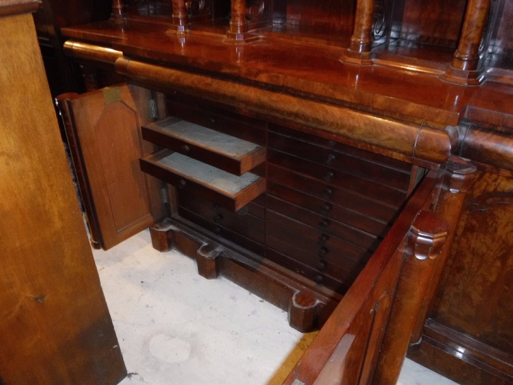 A large Regency mahogany side cabinet featuring turned support columns, panelled cupboard doors, and a tier of raised shelves. View IX