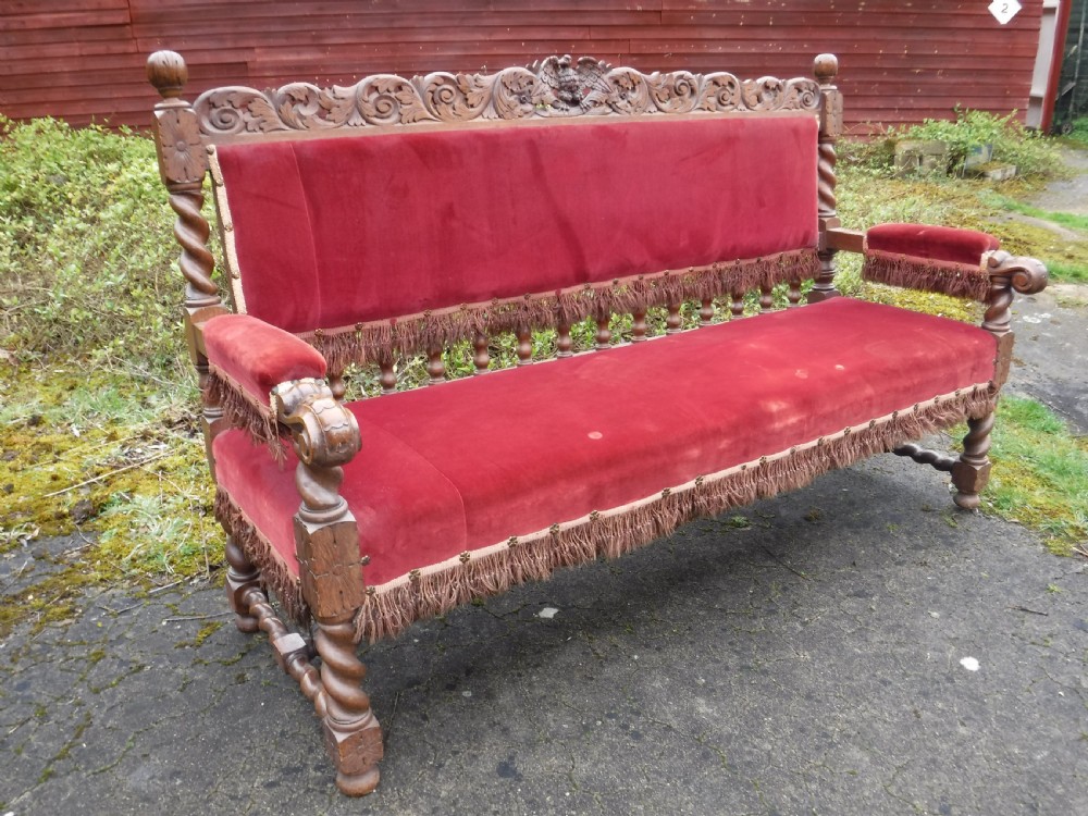 A late nineteenth-century carved oak hall bench featuring red velvet upholstery with fringe trim and barley twist legs.