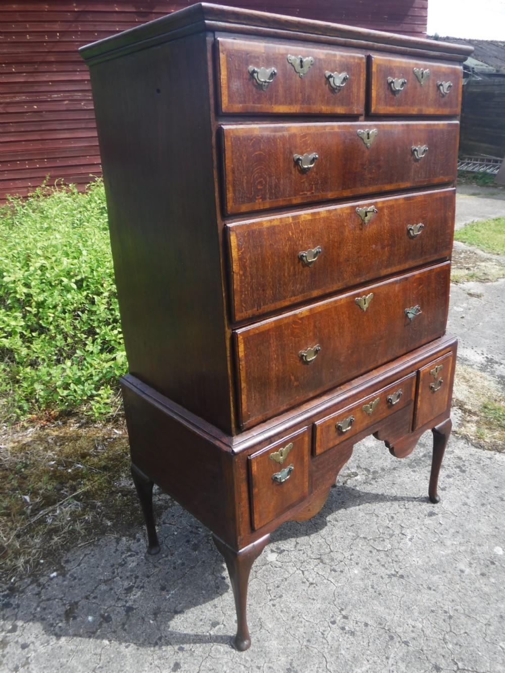 An early eighteenth-century oak chest on stand featuring crossbanded drawer fronts, brass drop handles, keyhole escutcheons, a shaped apron, and cabriole legs with pad feet. View III
