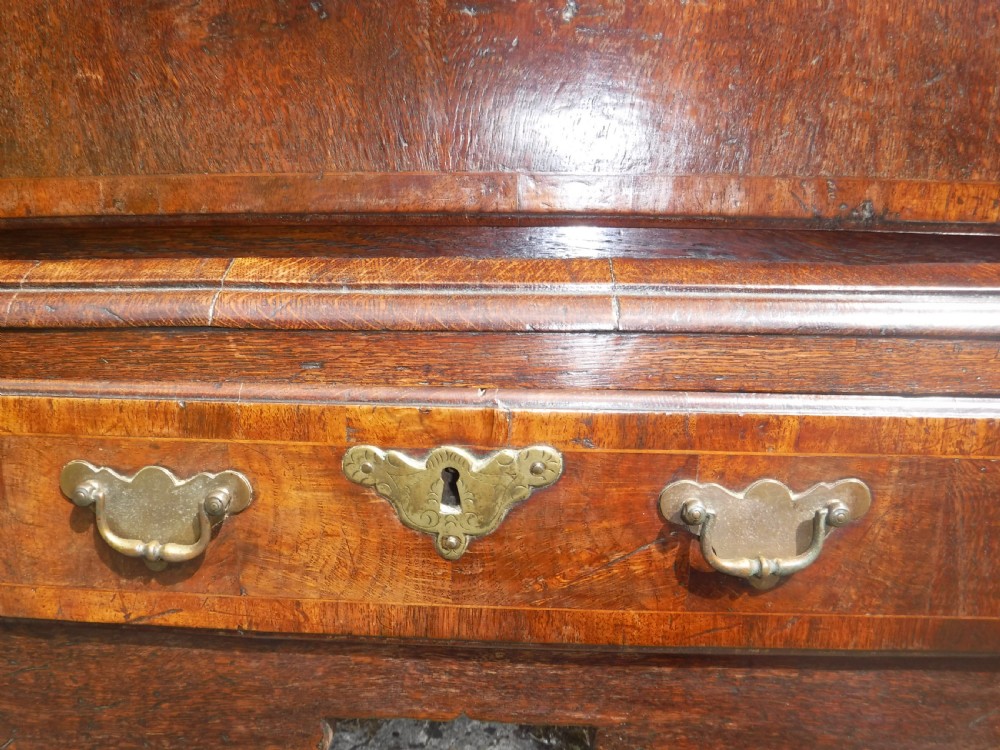 An early eighteenth-century oak chest on stand featuring crossbanded drawer fronts, brass drop handles, keyhole escutcheons, a shaped apron, and cabriole legs with pad feet. View VII