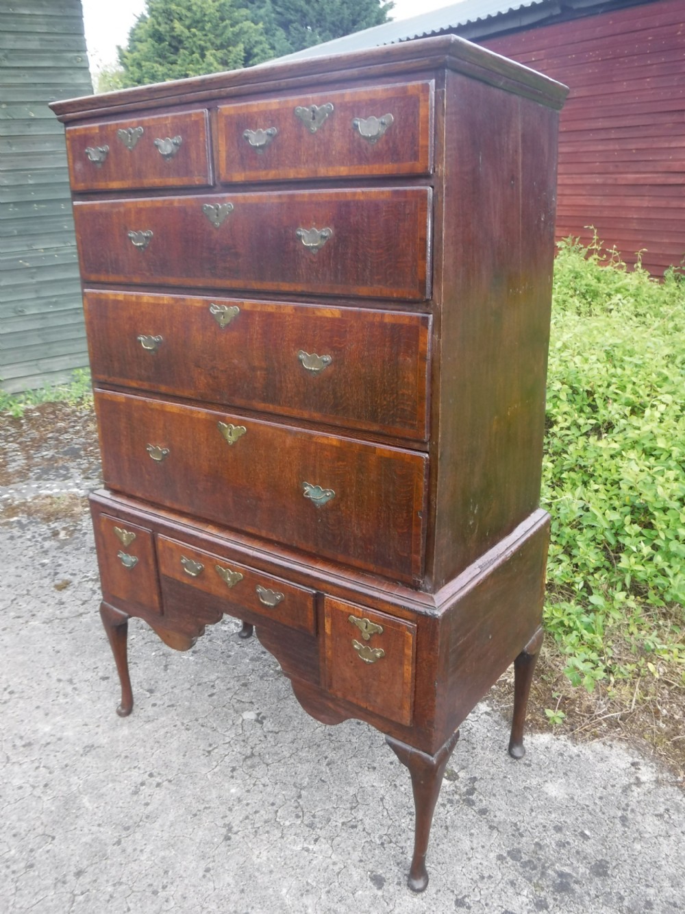 An early eighteenth-century oak chest on stand featuring crossbanded drawer fronts, brass drop handles, keyhole escutcheons, a shaped apron, and cabriole legs with pad feet. View X