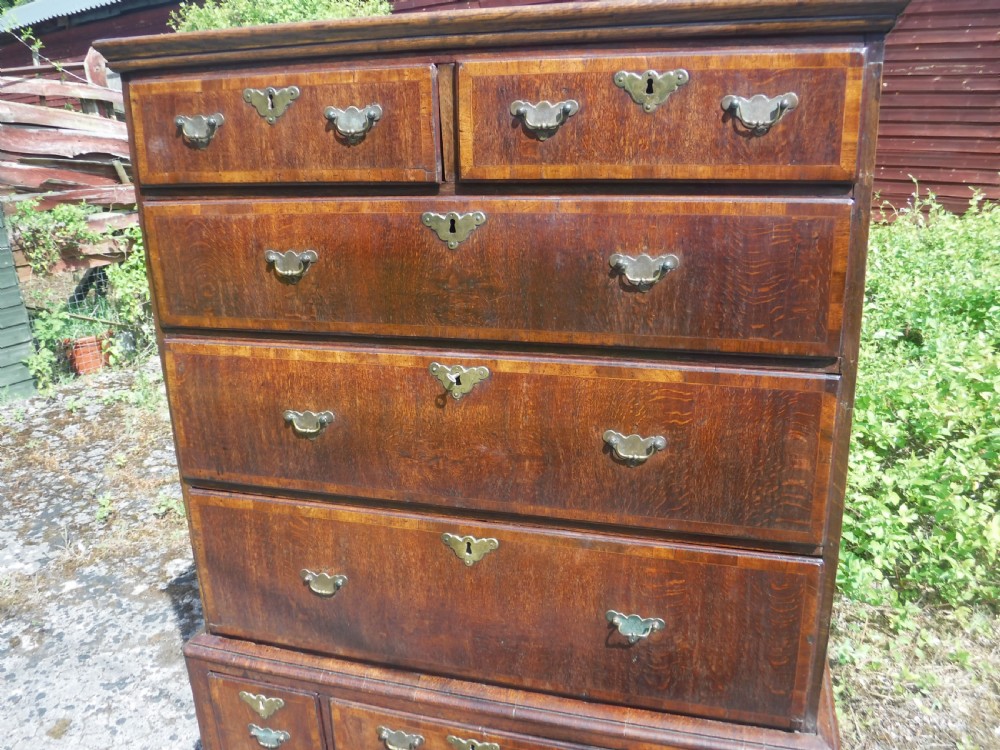 An early eighteenth-century oak chest on stand featuring crossbanded drawer fronts, brass drop handles, keyhole escutcheons, a shaped apron, and cabriole legs with pad feet. View XI