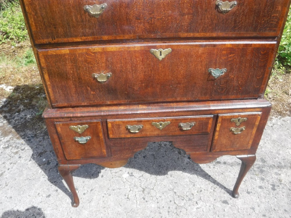 An early eighteenth-century oak chest on stand featuring crossbanded drawer fronts, brass drop handles, keyhole escutcheons, a shaped apron, and cabriole legs with pad feet. View XII