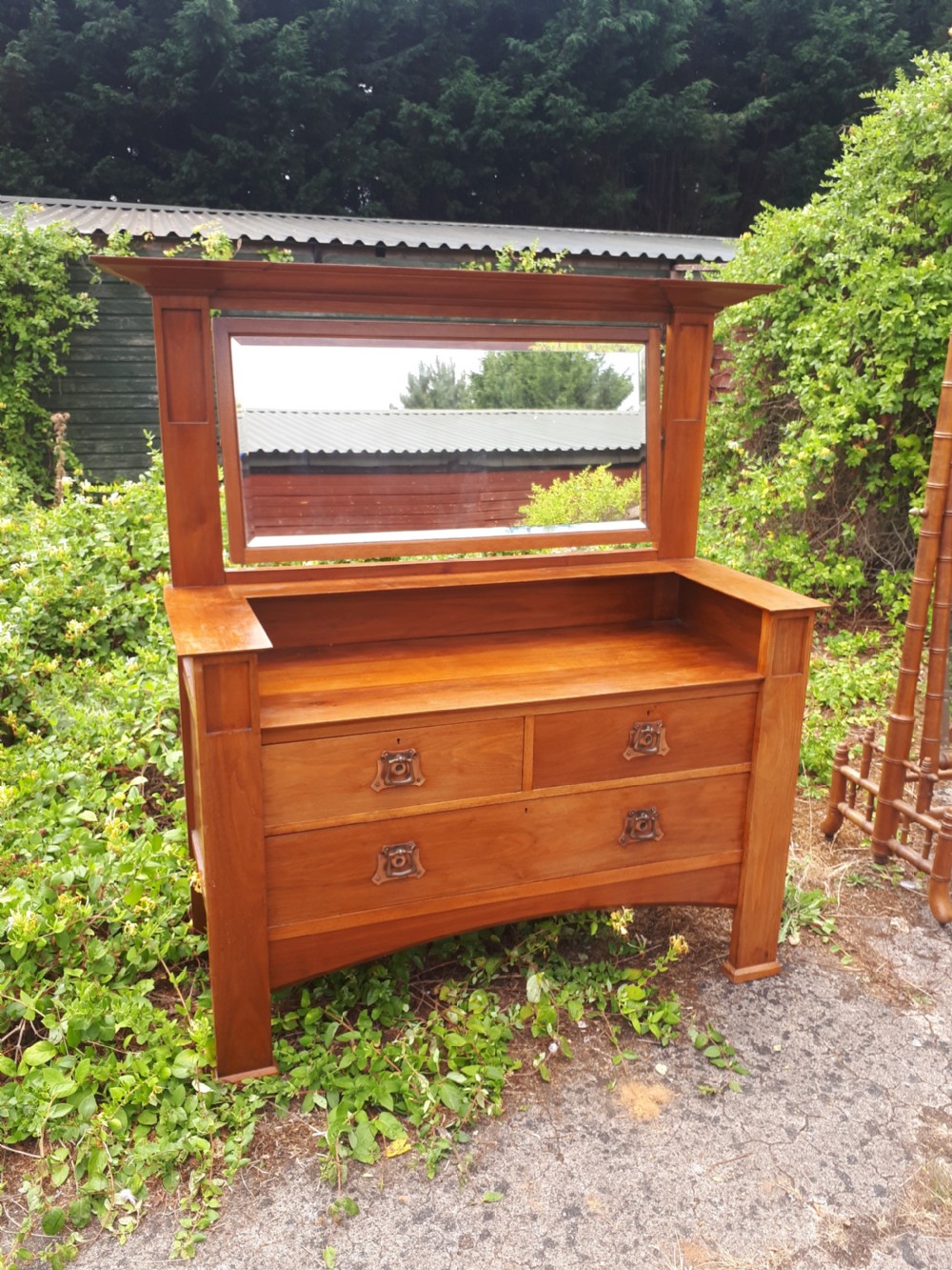 A late nineteenth-century Arts and Crafts wooden dressing chest featuring an integrated mirror, upper mantle shelf, two short drawers, one long drawer, and copper backplate handles.
