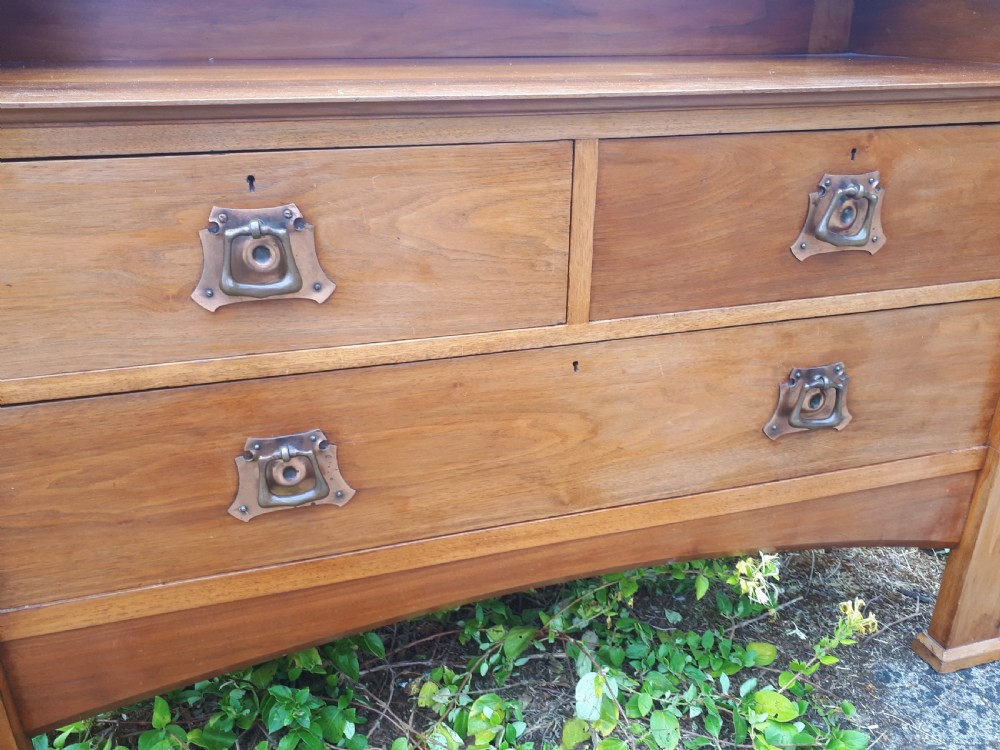 A late nineteenth-century Arts and Crafts wooden dressing chest featuring an integrated mirror, upper mantle shelf, two short drawers, one long drawer, and copper backplate handles. View V