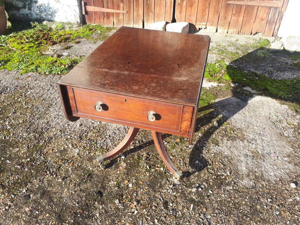 A Regency mahogany sofa table with brass line inlay, drop leaves, a single drawer, and splayed legs resting on brass castors.