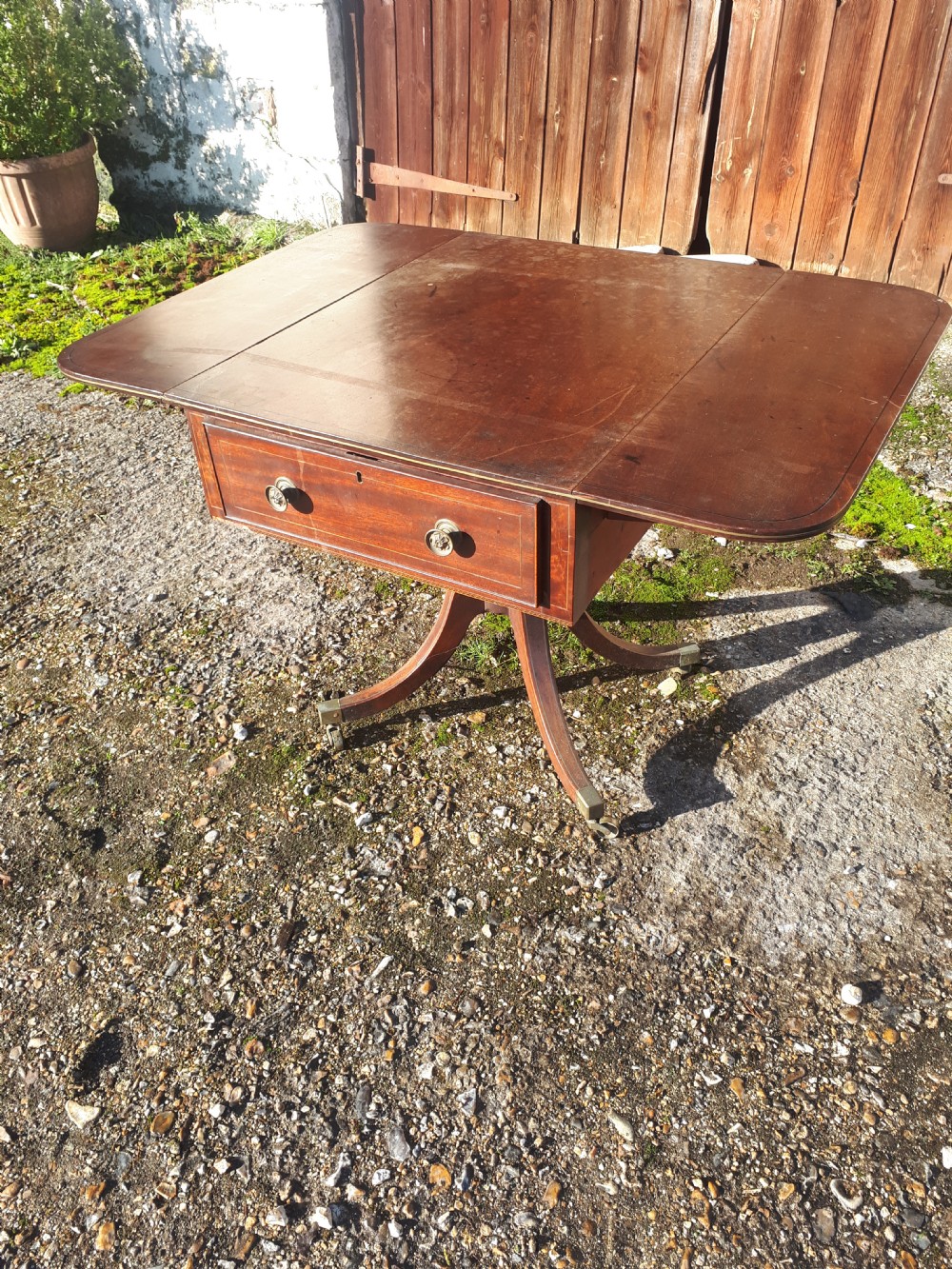 A Regency mahogany sofa table with brass line inlay, drop leaves, a single drawer, and splayed legs resting on brass castors. View III