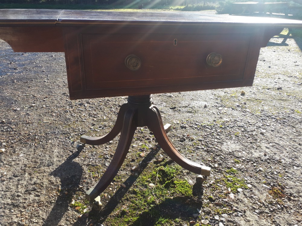 A Regency mahogany sofa table with brass line inlay, drop leaves, a single drawer, and splayed legs resting on brass castors. View V