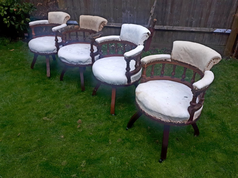 A set of four late nineteenth-century oak revolving desk armchairs featuring turned spindles, splayed legs on castors, and calico upholstery.