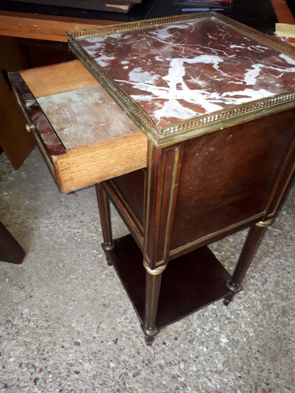 A 19th-century mahogany bedside cabinet featuring a red veined marble top with a brass gallery, a single drawer, a cupboard door, brass inlay trim, and fluted legs with an open lower shelf. View VI