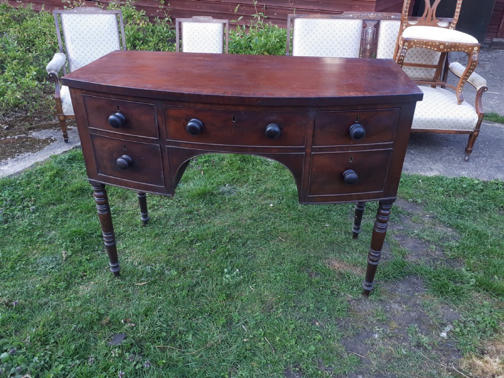 A nineteenth-century Regency mahogany bow-fronted sideboard featuring five drawers with turned wooden knobs and four turned legs.