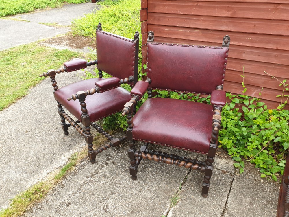 A pair of late 19th-century dark oak armchairs featuring barley twist legs and stretchers, carved finials, and burgundy leather upholstery secured with decorative brass studs.