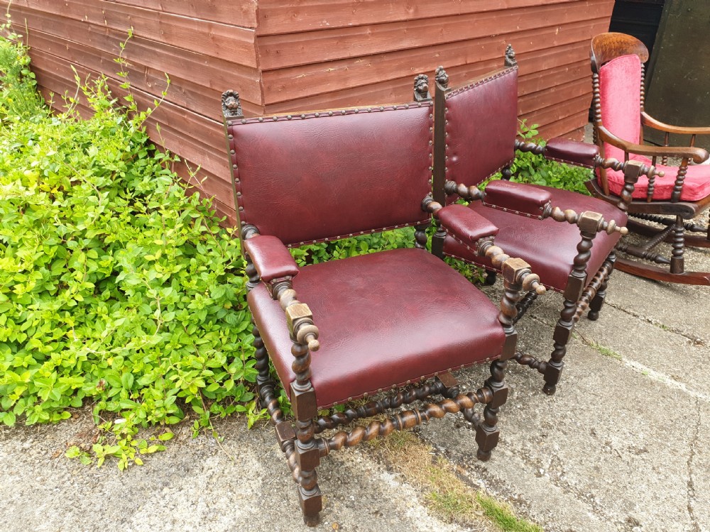 A pair of late 19th-century dark oak armchairs featuring barley twist legs and stretchers, carved finials, and burgundy leather upholstery secured with decorative brass studs. View II