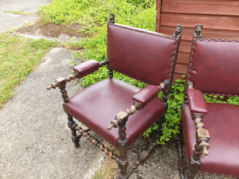 A pair of late 19th-century dark oak armchairs featuring barley twist legs and stretchers, carved finials, and burgundy leather upholstery secured with decorative brass studs. View V
