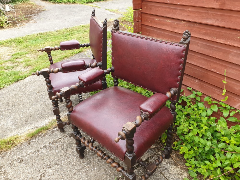 A pair of late 19th-century dark oak armchairs featuring barley twist legs and stretchers, carved finials, and burgundy leather upholstery secured with decorative brass studs. View VI