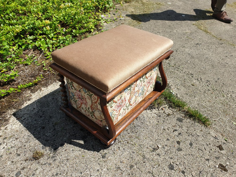 An early Victorian rosewood box seat stool with a brown padded cushion seat, floral upholstered fabric side panels, and shaped wooden supports.