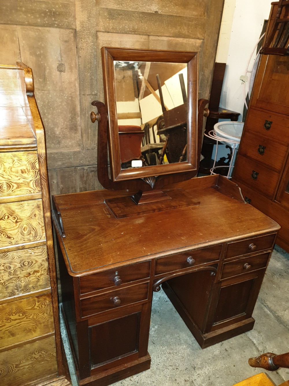 Mid-19th-century mahogany kneehole dressing table featuring an integrated rectangular swivel mirror, turned wooden knobs, and twin pedestal drawer bases.