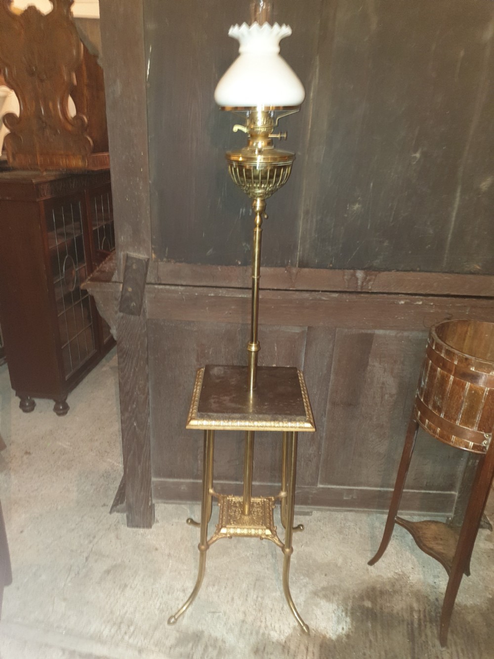 A Victorian brass floor lamp featuring an integrated square tier, splayed legs, and a white frilled milk glass shade.