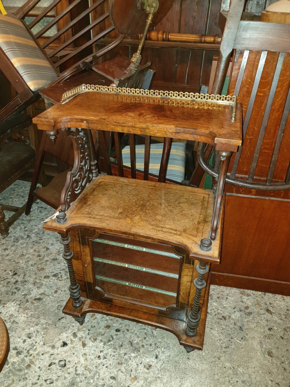 A Victorian burr walnut music cabinet featuring an upper shelf with a pierced brass gallery rail, turned upright columns, marquetry inlay, and a glass door opening to labelled shelves.