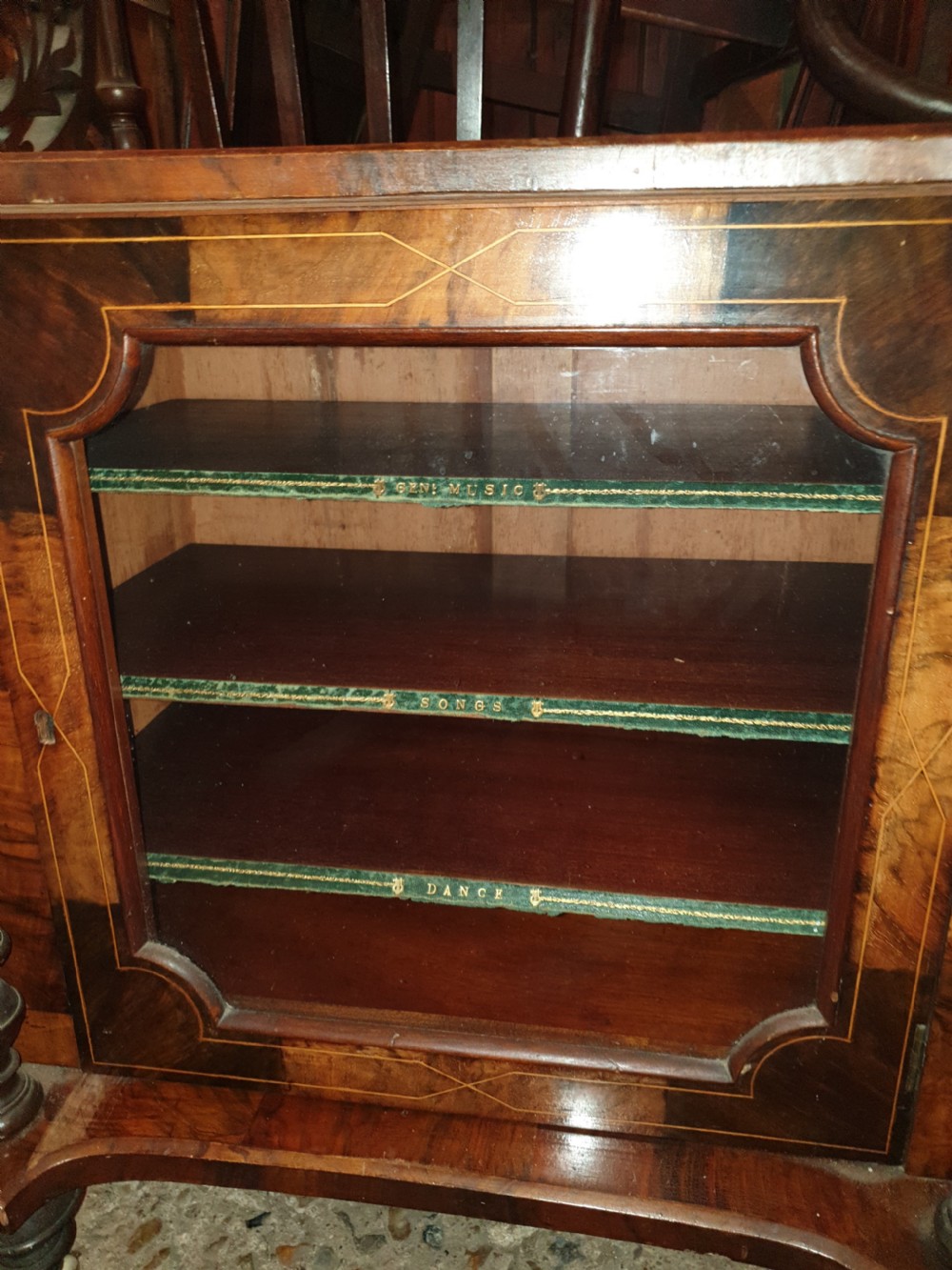 A Victorian burr walnut music cabinet featuring an upper shelf with a pierced brass gallery rail, turned upright columns, marquetry inlay, and a glass door opening to labelled shelves. View III