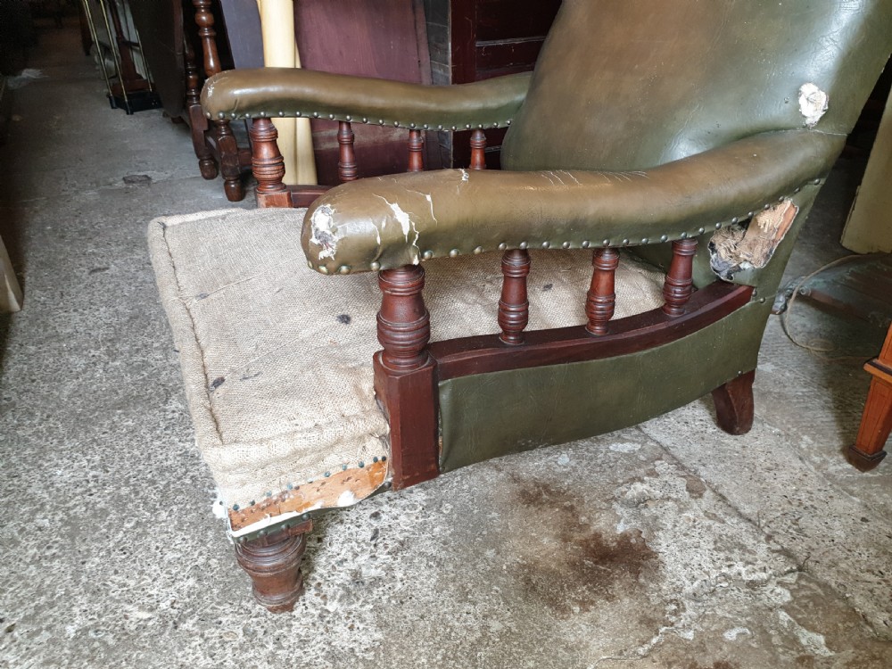 A deep Victorian Howard style armchair upholstered in worn olive green leather with turned wooden spindles under the armrests and turned front legs. View II