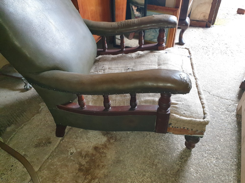 A deep Victorian Howard style armchair upholstered in worn olive green leather with turned wooden spindles under the armrests and turned front legs. View III