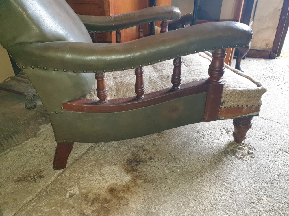 A deep Victorian Howard style armchair upholstered in worn olive green leather with turned wooden spindles under the armrests and turned front legs. View IV
