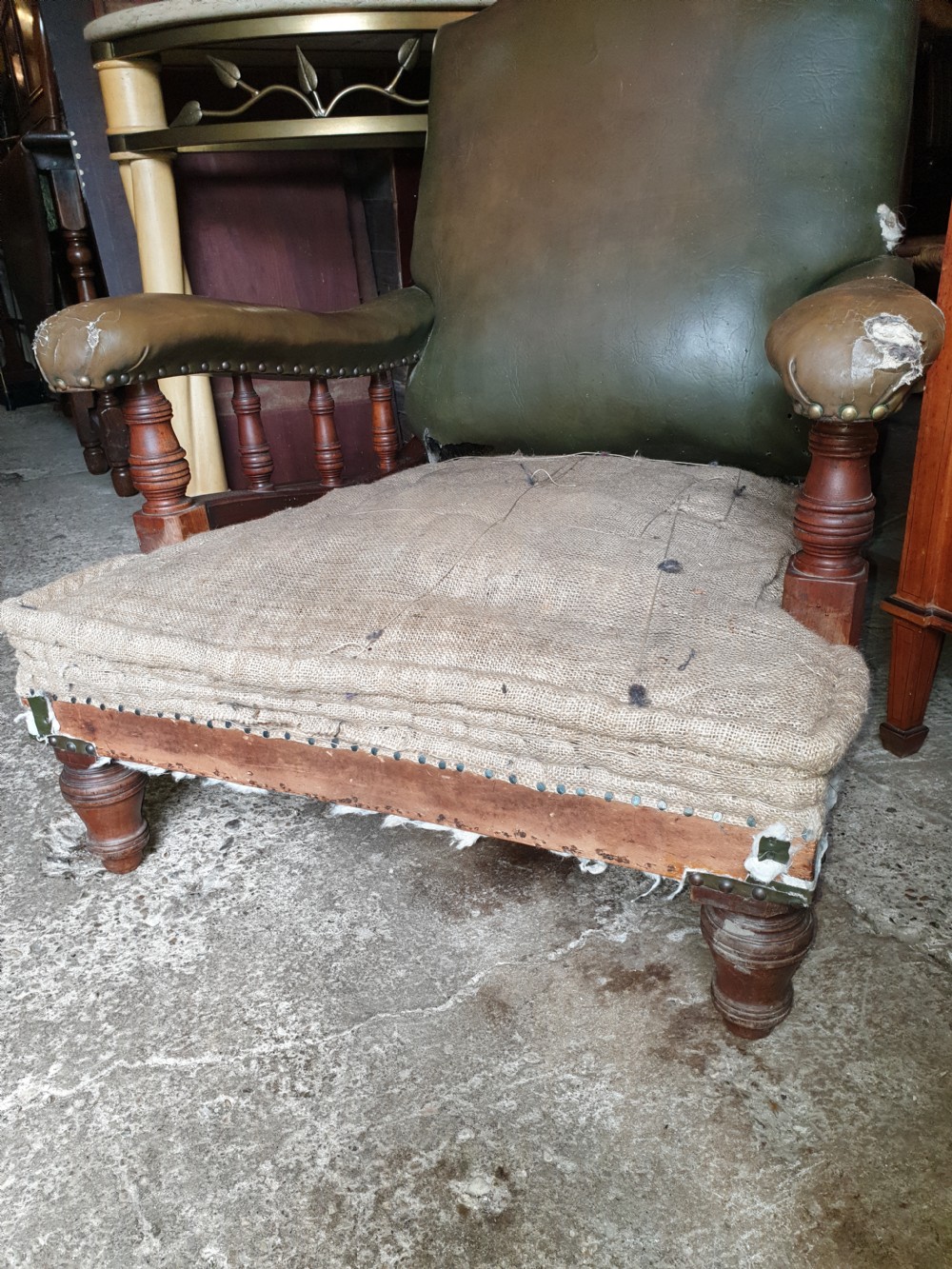 A deep Victorian Howard style armchair upholstered in worn olive green leather with turned wooden spindles under the armrests and turned front legs. View V