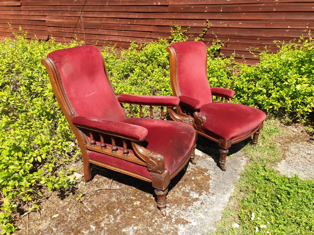 A pair of Victorian armchairs upholstered in crimson red velvet with turned wooden spindle armrests and brass castors.