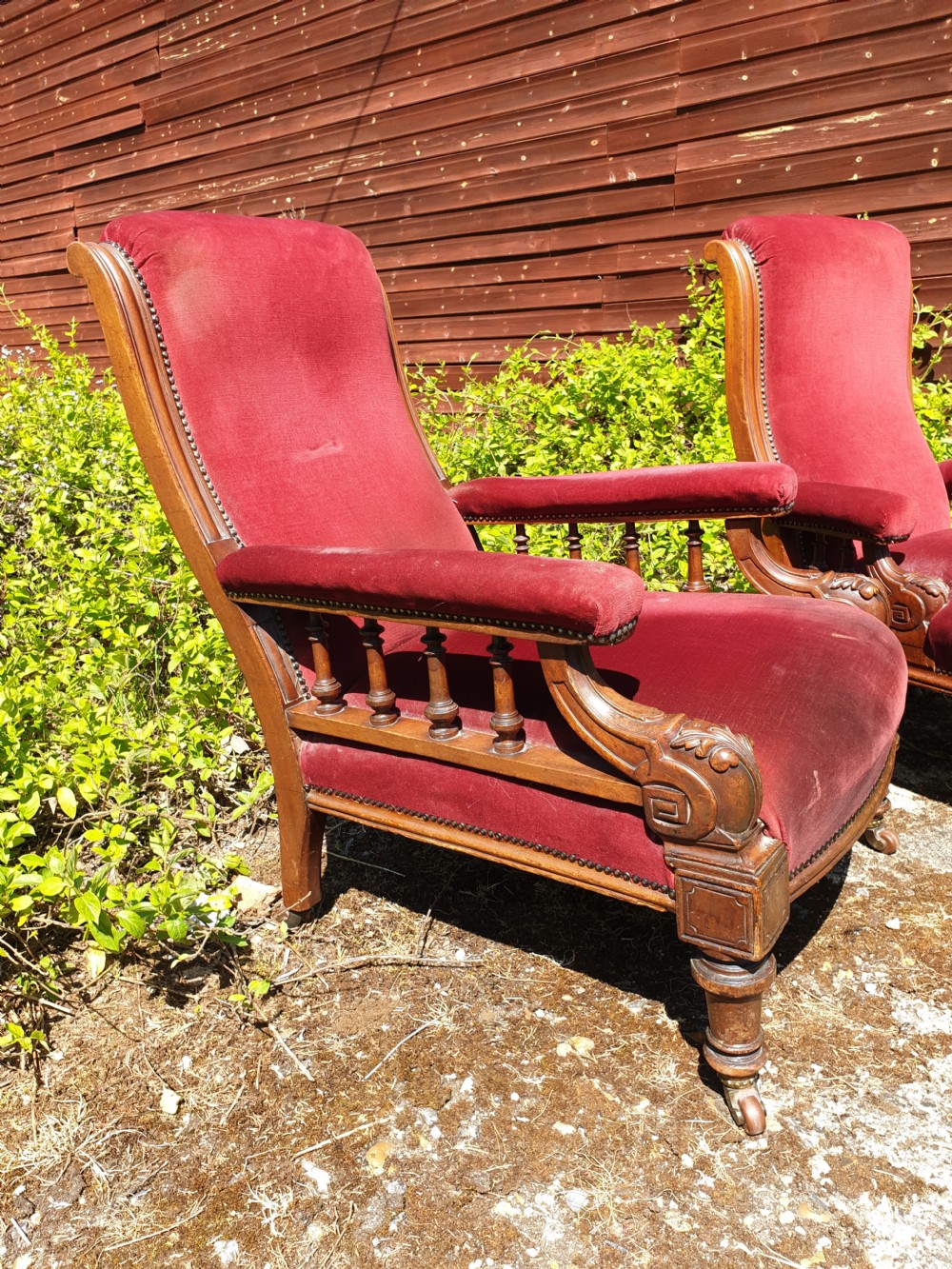 A pair of Victorian armchairs upholstered in crimson red velvet with turned wooden spindle armrests and brass castors. View II