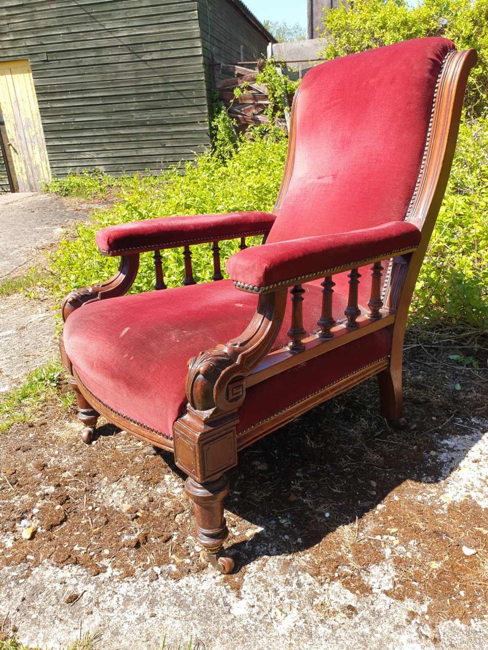 A pair of Victorian armchairs upholstered in crimson red velvet with turned wooden spindle armrests and brass castors. View V