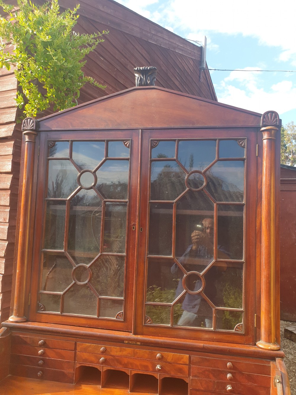 A Regency mahogany bureau bookcase featuring a pediment roof, two glazed cabinet doors with geometric astragal bars, a drop-down desk flap revealing interior drawers, and a lower double-door cupboard flanked by turned side columns. View II