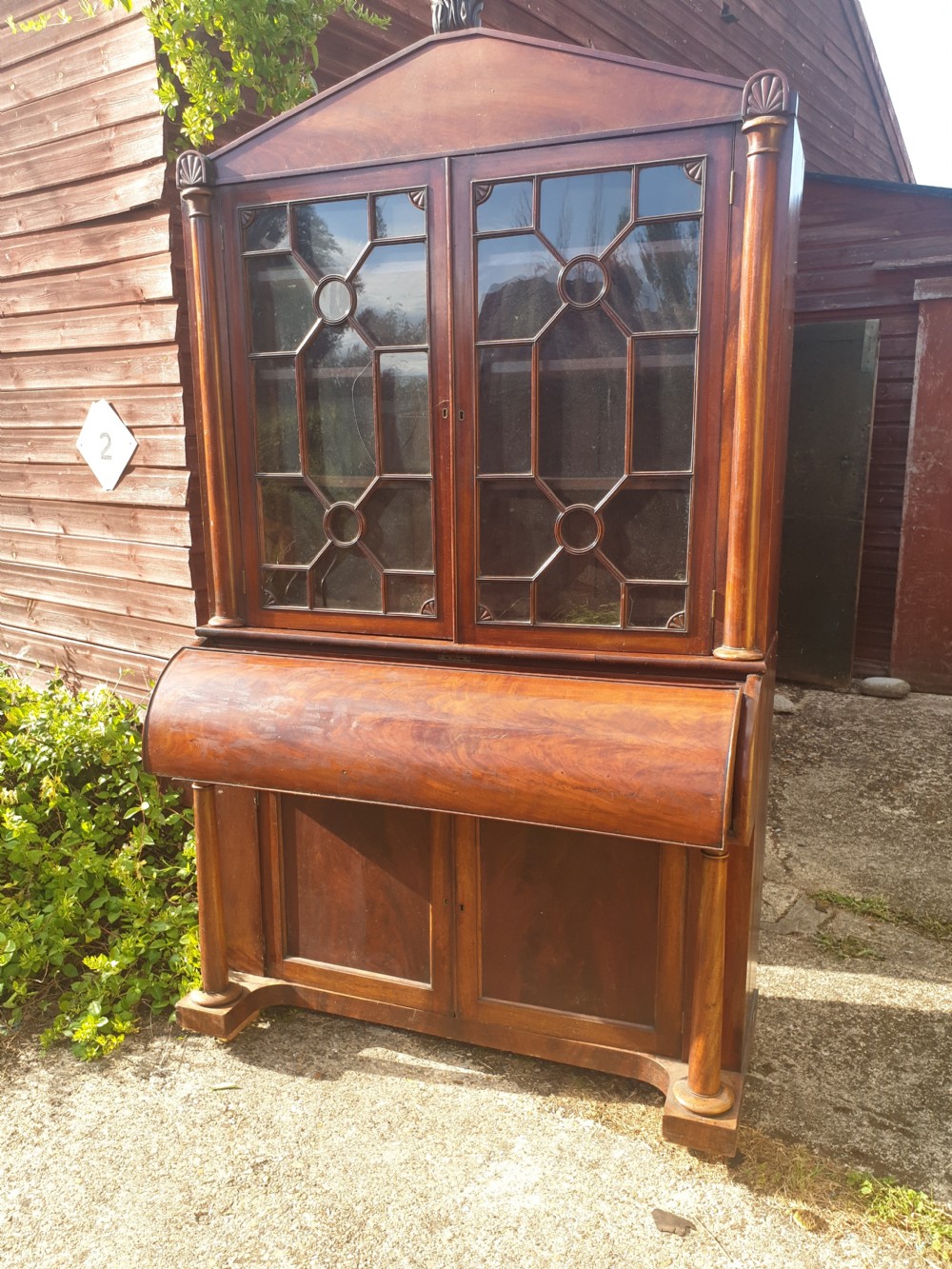 A Regency mahogany bureau bookcase featuring a pediment roof, two glazed cabinet doors with geometric astragal bars, a drop-down desk flap revealing interior drawers, and a lower double-door cupboard flanked by turned side columns. View V