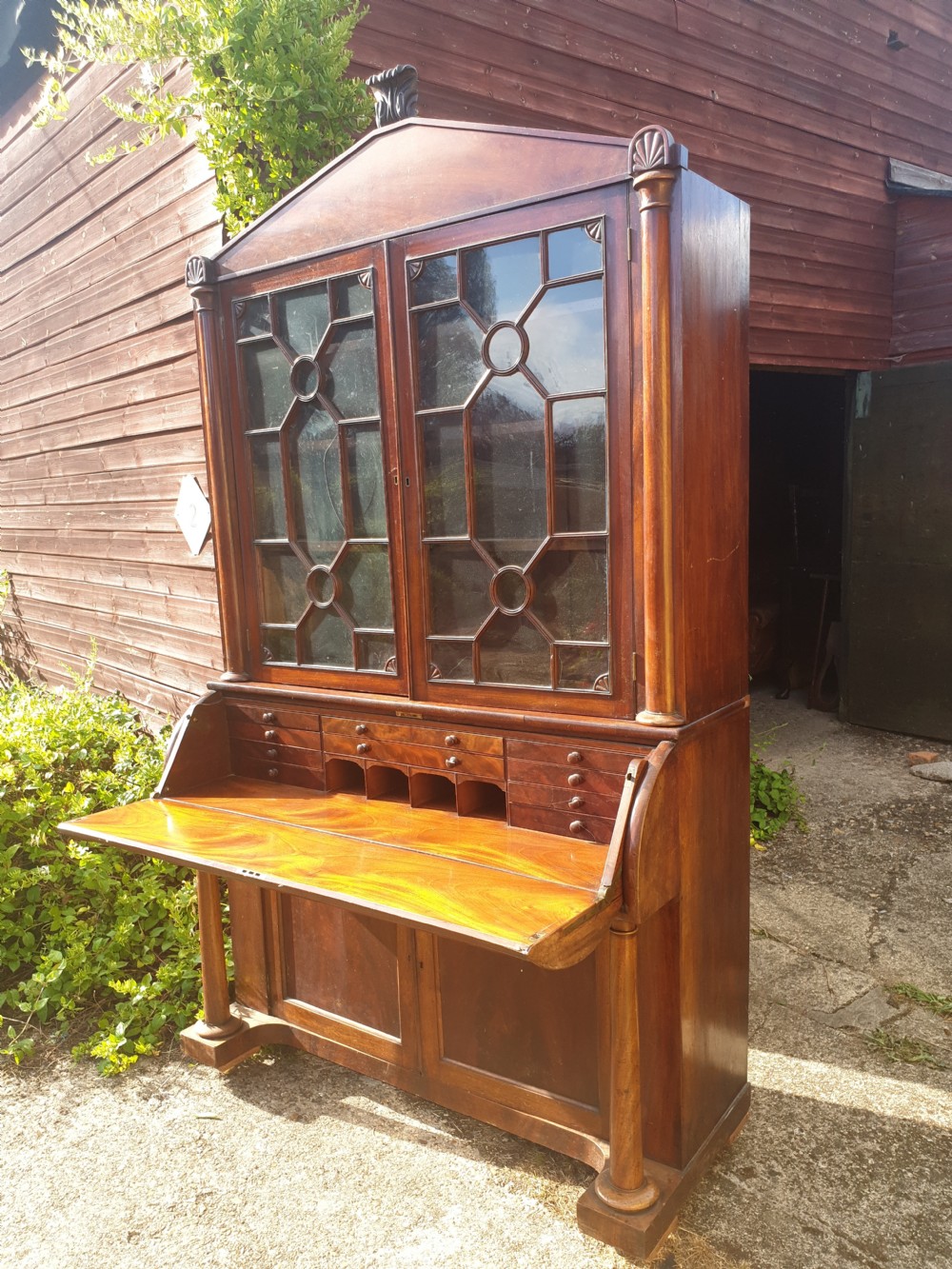 A Regency mahogany bureau bookcase featuring a pediment roof, two glazed cabinet doors with geometric astragal bars, a drop-down desk flap revealing interior drawers, and a lower double-door cupboard flanked by turned side columns. View VI
