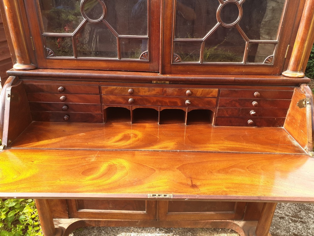 A Regency mahogany bureau bookcase featuring a pediment roof, two glazed cabinet doors with geometric astragal bars, a drop-down desk flap revealing interior drawers, and a lower double-door cupboard flanked by turned side columns. View IX