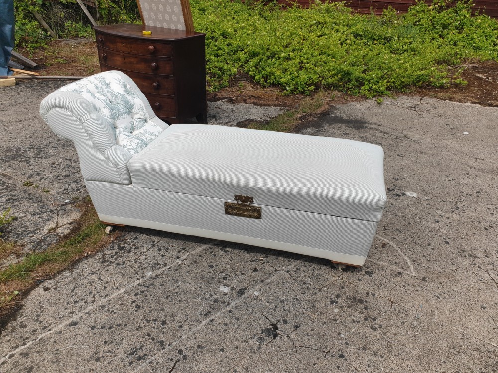 A late Victorian box ottoman chaise longue upholstered in grey and white ticking stripe fabric featuring a button-tufted backrest and a brass front latch.